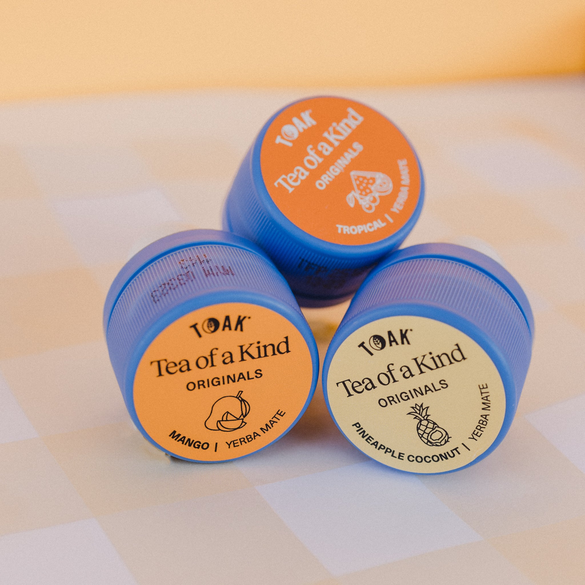 Three caps of TOAK tropical yerba mate on a checkered fabric background