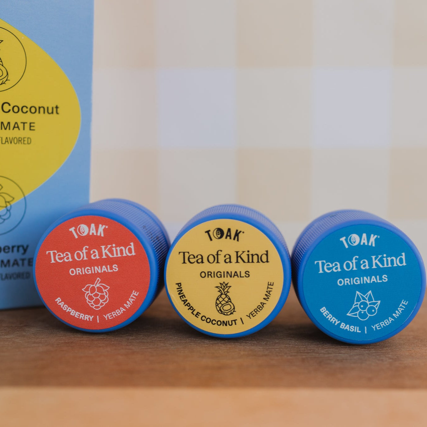 Three caps of TOAK yerba mate with colorful labels on a wooden surface.