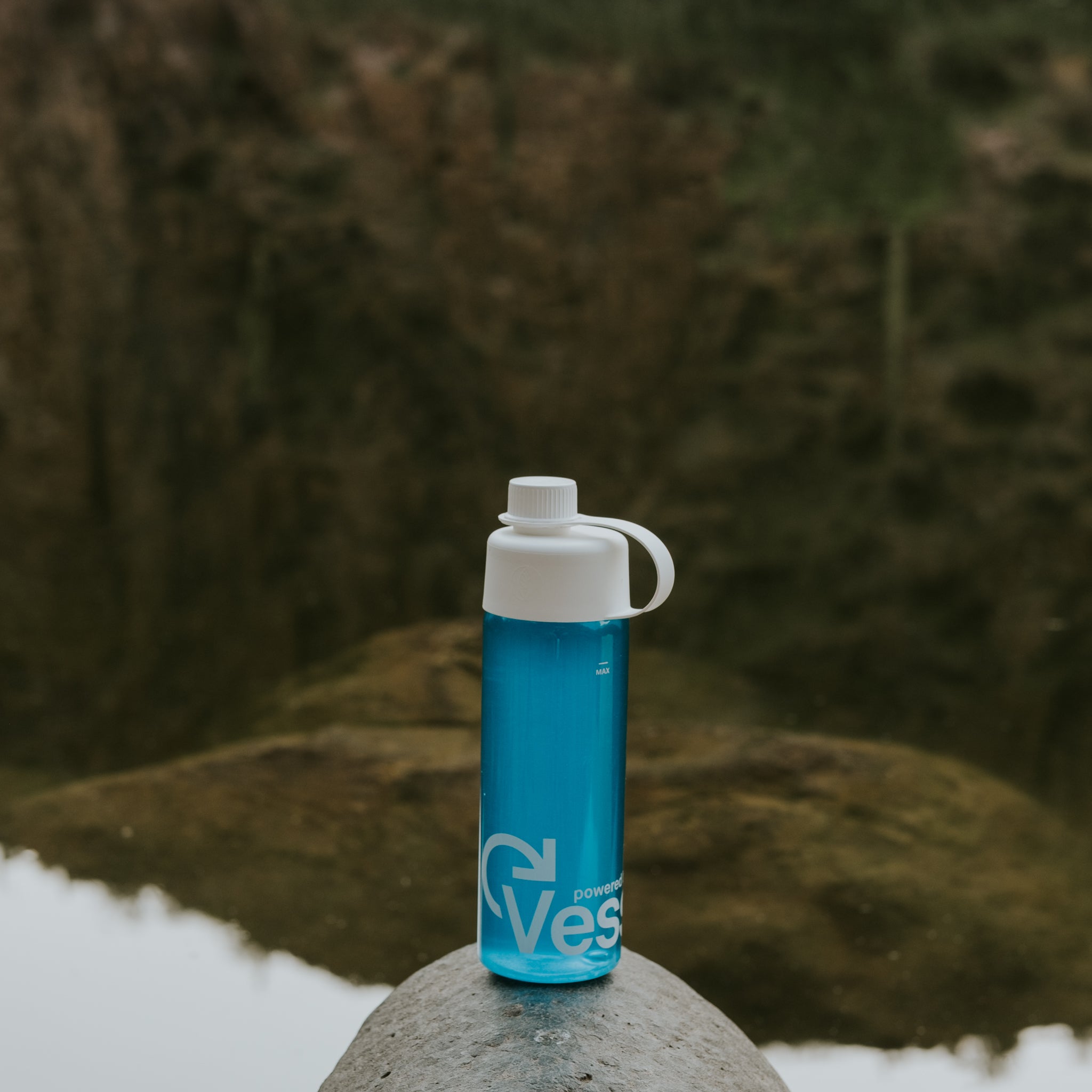 Blue water bottle with white cap on a rock in a natural setting