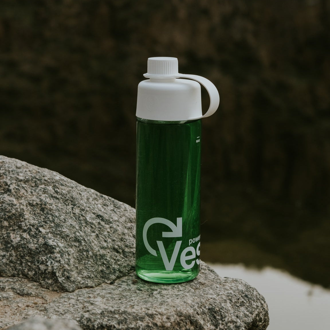 Green water bottle with white cap on a rock by a river